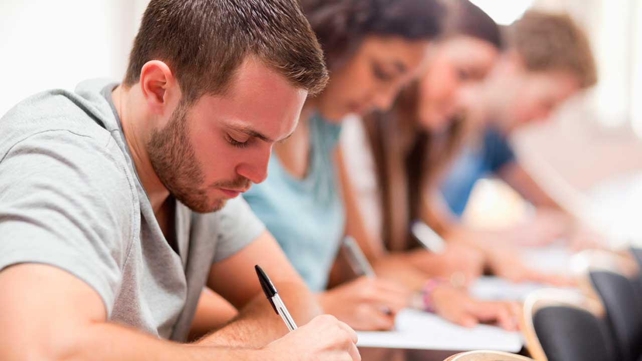 Focused students sit in a row, writing in notebooks
