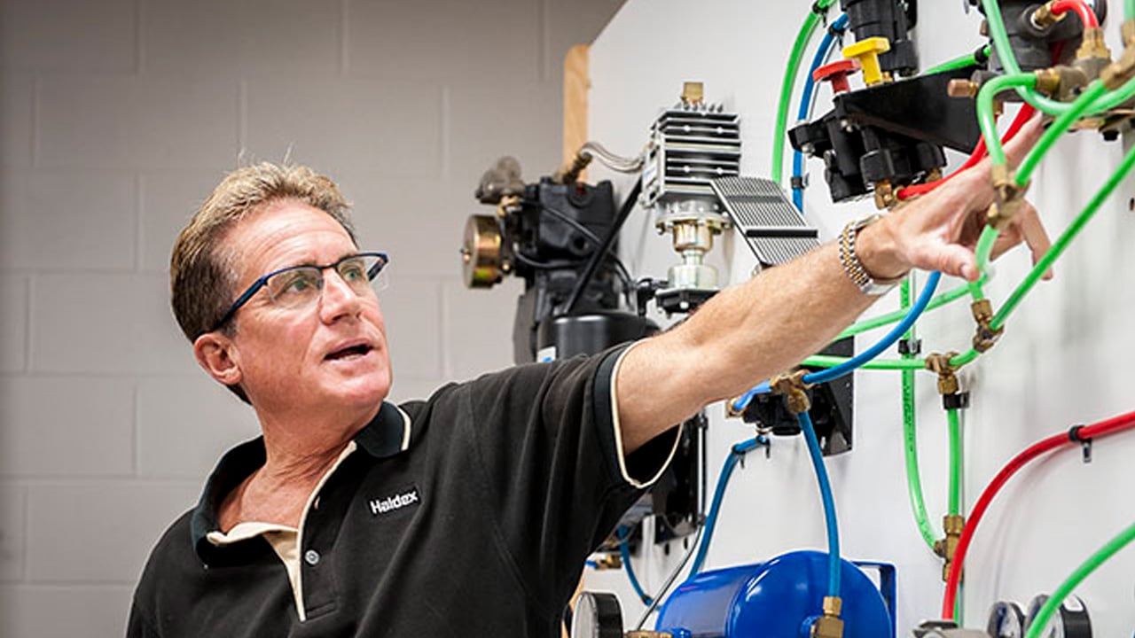 Man points at a complex system of colored air brake hoses on a training wall