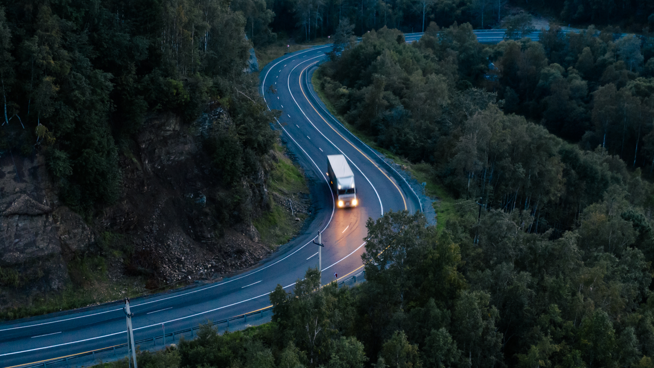 Truck driving on a winding forest road at dusk with headlights on